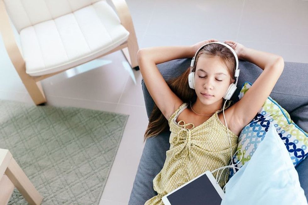 0 years old tween girl relaxing on a couch, listening to music in headphones and playing with tablet pc
