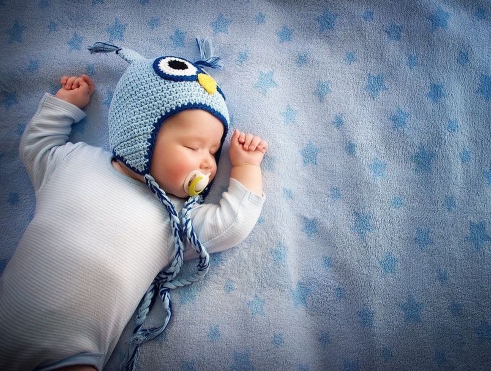 4 month old baby in owl hat sleeping on blue blanket.