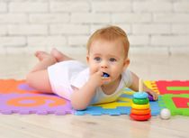 A 7-month-old baby plays on the floor with toys and stuffs