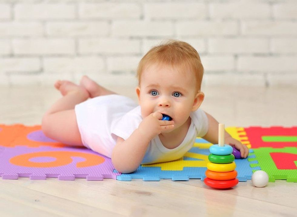 A 7-month-old baby plays on the floor with toys and stuffs