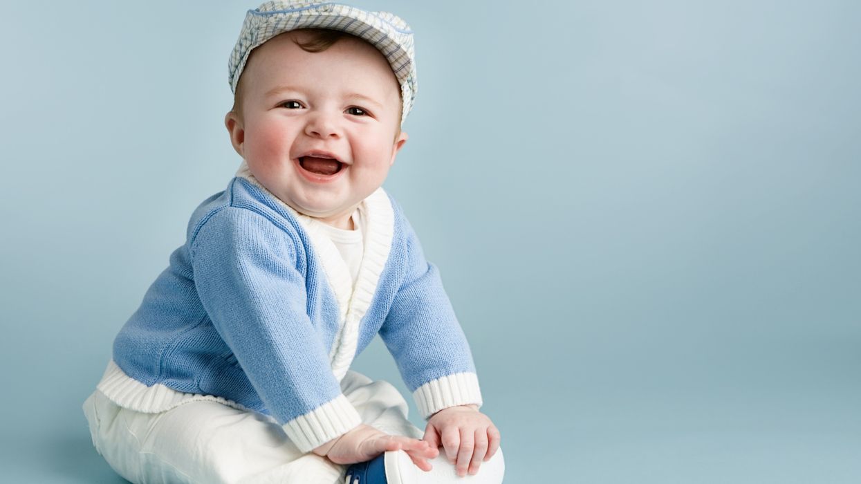 A baby boy dressed in blue and white attire, laughing. 