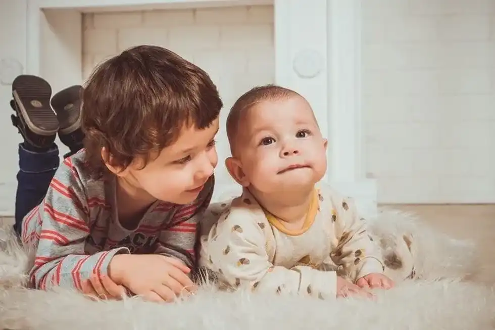 A baby boy laying on fur with his elder brother