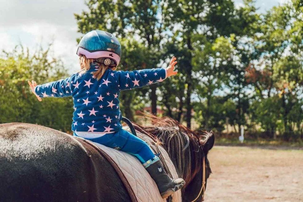 A baby girl sitting on a horse without holding the leash
