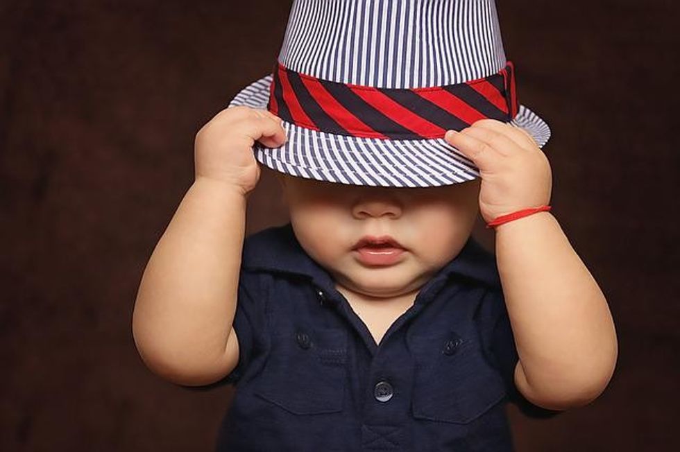 A baby wearing a striped hat covering their eyes, symbolizing funky names for children.
