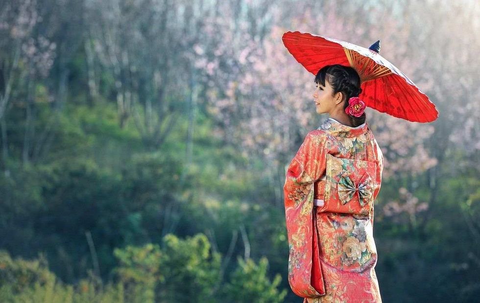 A beautiful lady dressed in Japanese cultural attire, holding an umbrella and standing against a nature backdrop