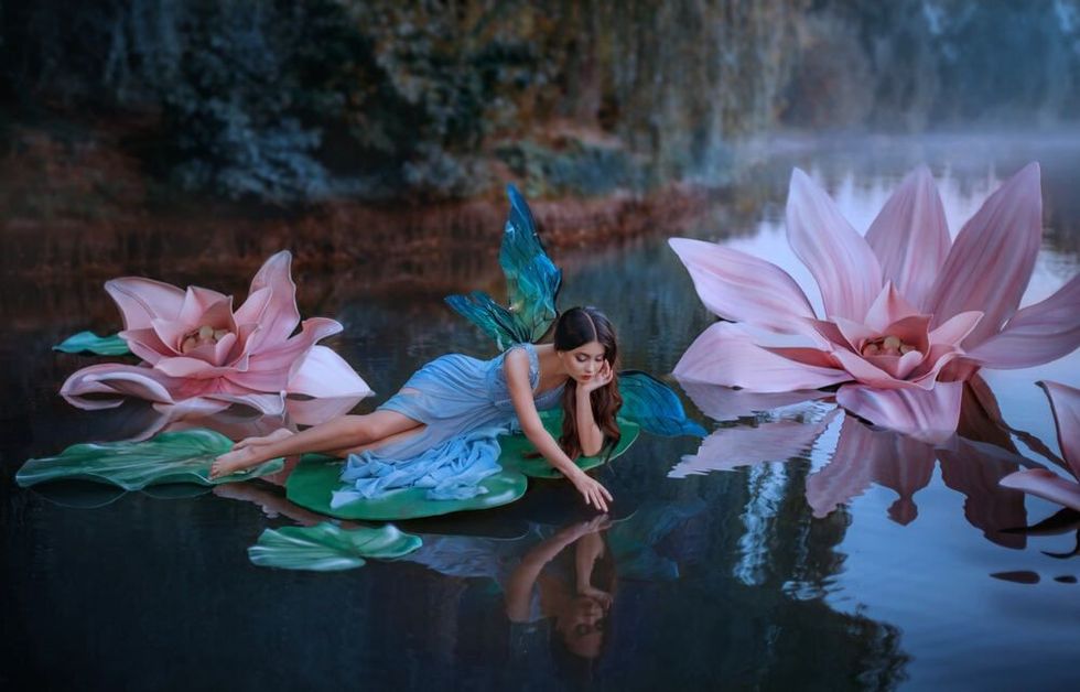 A beautiful woman a little cute fairy with butterfly wings lies on green water lily leaf