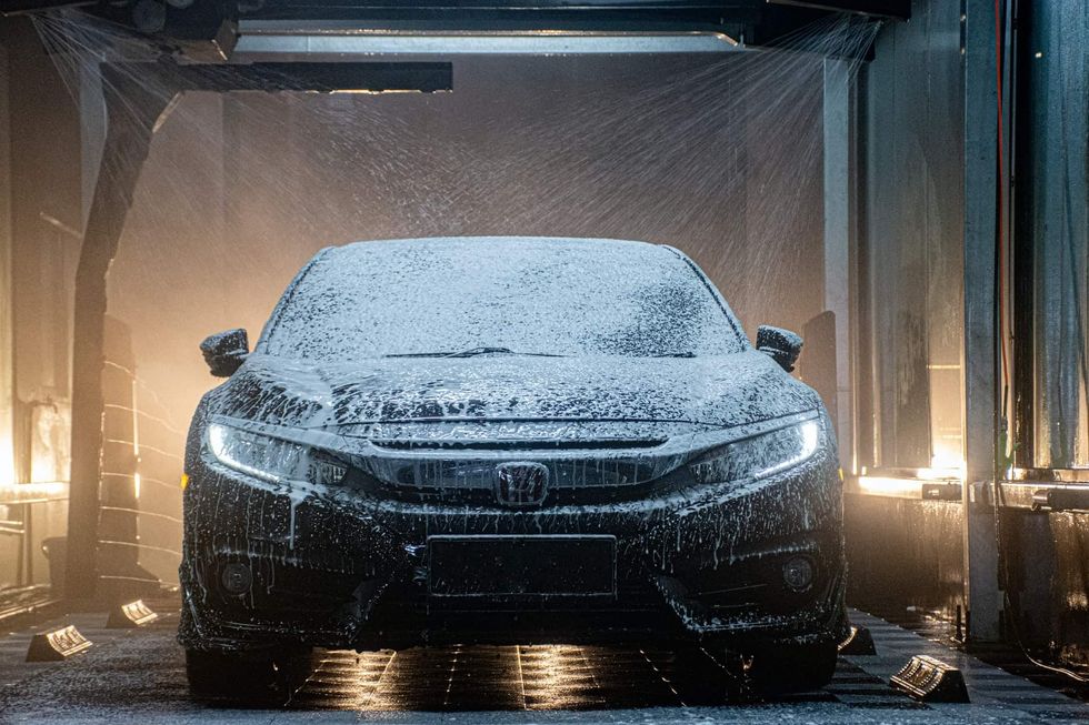 A black car covered in a spray of soapy water at a carwash