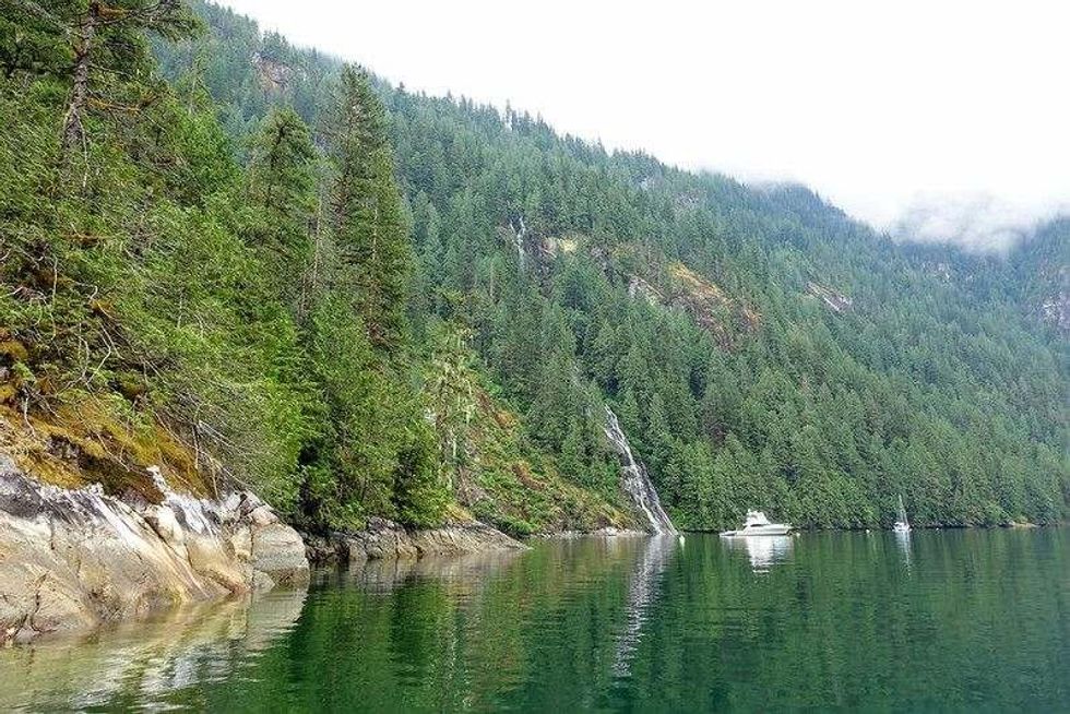 A boat anchored in front of a beautiful waterfall surrounded by rugged forests