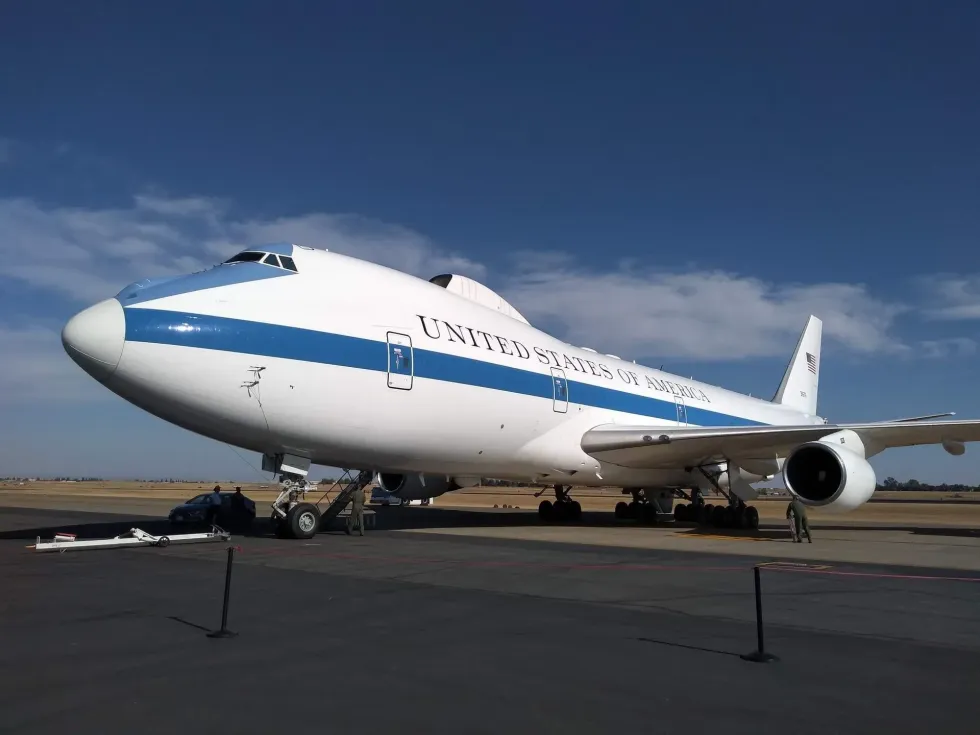 A Boeing 747 aircraft labeled 'UNITED STATES OF AMERICA' parked on the tarmac with clear skies in the background.