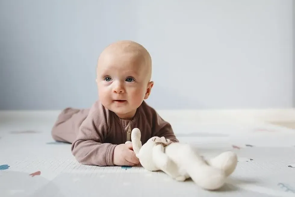 A boy lying down on his belly and playing with a teddy bear.