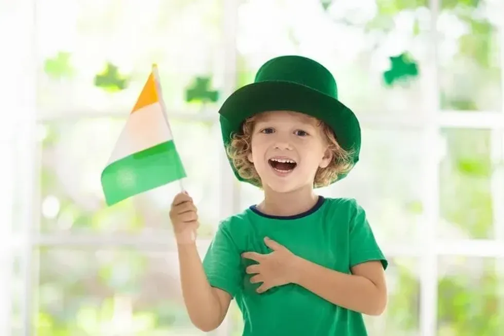 A boy wearing green hat and holding flag of Ireland