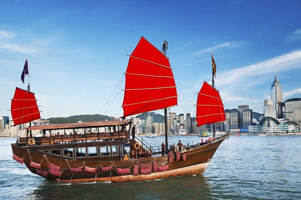 A brown ship with red sails sailing towards the harbour