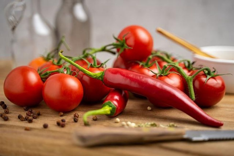 A bunch of chili peppers and tomatoes set on a wooden table with a knife.