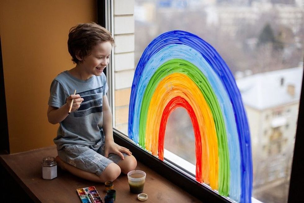 A child at home painting a rainbow on the window.