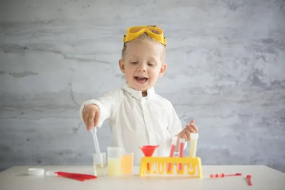 A child in a laboratory coat and a pair of googles playing with science equipment.