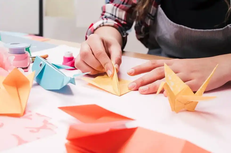 A child's hands folding paper to make an origami monkey, surrounded by lots of other origami animal models.