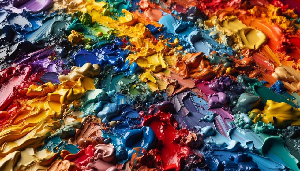 A close-up view of various glossy paint colors blending together in an abstract, colorful mix on a landscape canvas.
