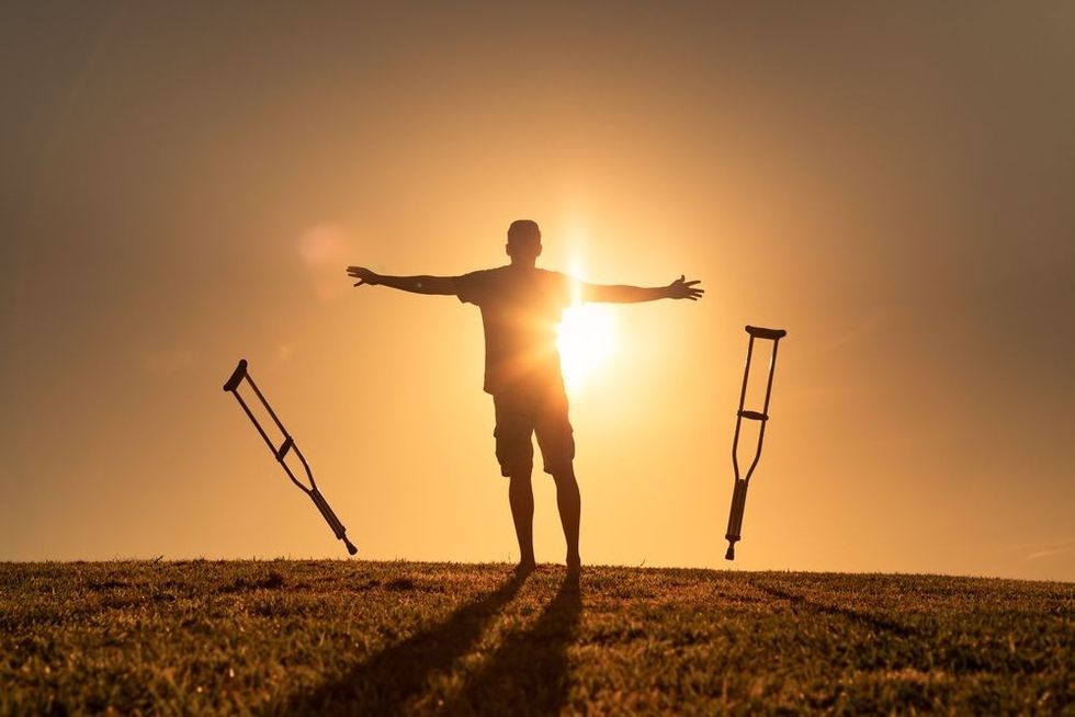 A disabled man letting go of his crutches facing the sunset.