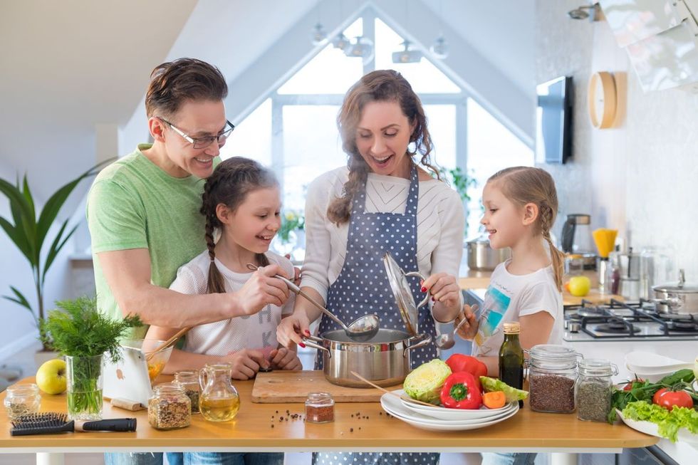 A family of four cooking in a kitchen with different ingredients scattered across the table, including chili