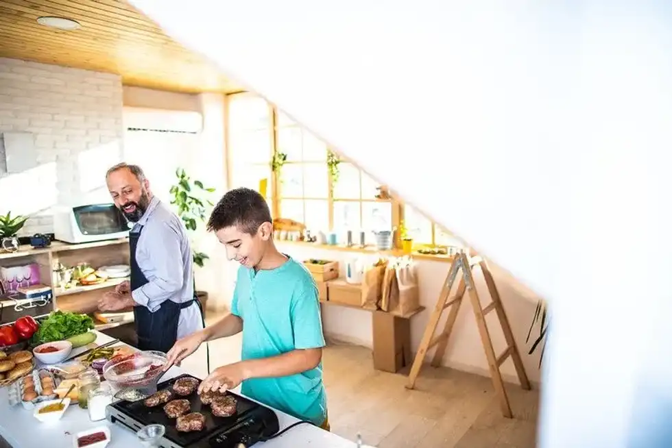 A father teaching his son how to BBQ indoors.