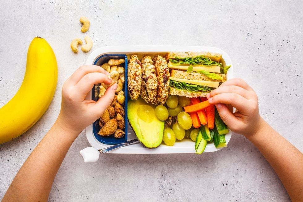 A food box with sandwich cookies nuts fruits and avocado.