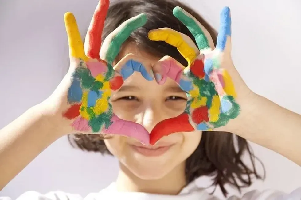 A girl making a heart sign with her painted hands