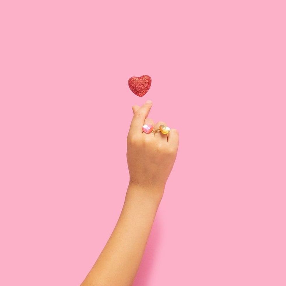 A girl's hand making a popular Kpop heart gesture.