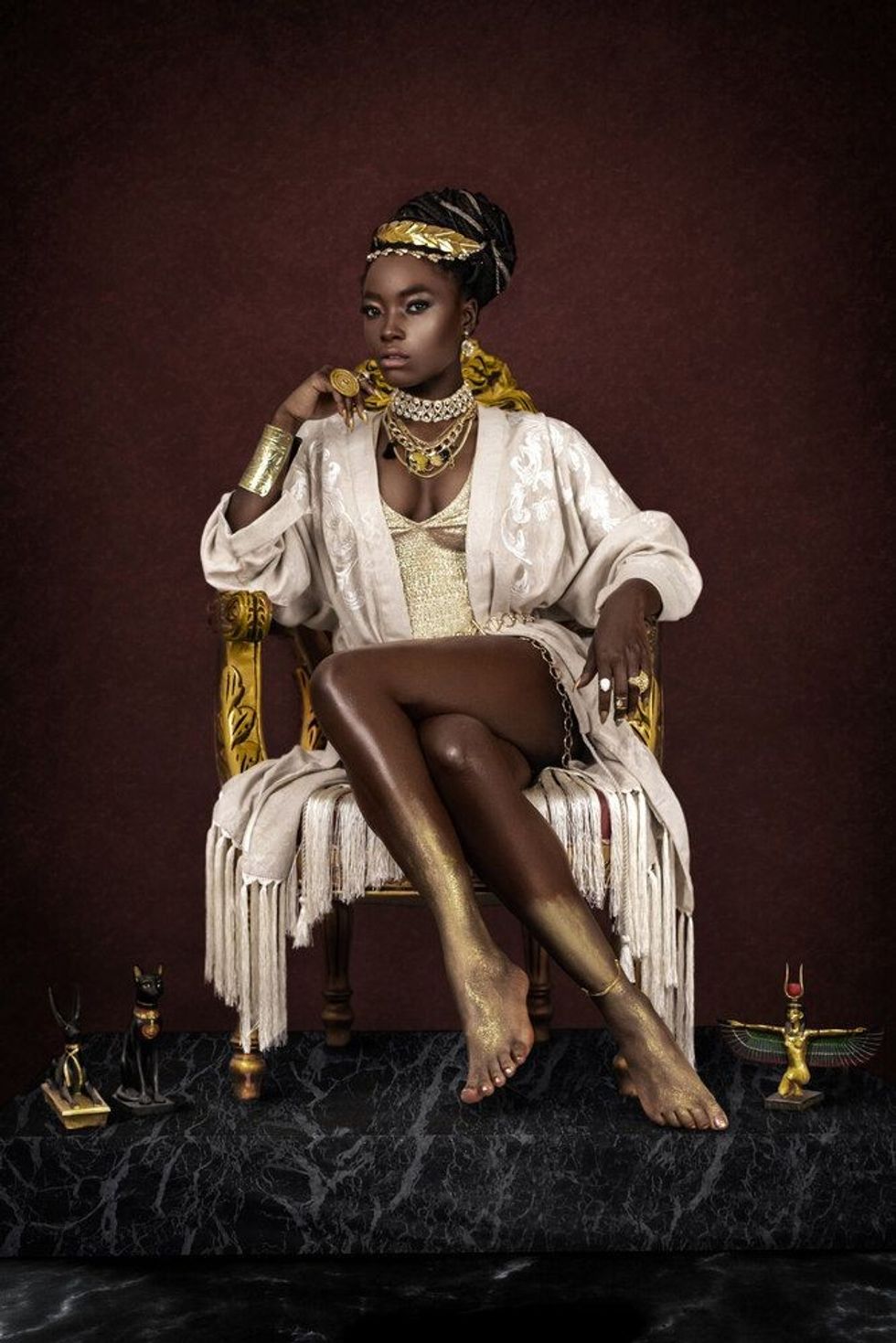 A gorgeous young female Egyptian Pharaoh wearing elegant clothing, a gold crown and jewelry is sitting on her golden throne.