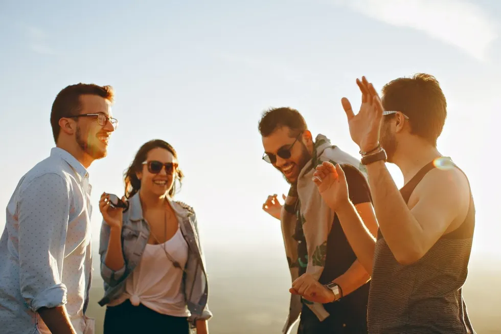 A group of friends enjoying a sunny outdoor gathering, laughing together, possibly over henway jokes and pun traps.