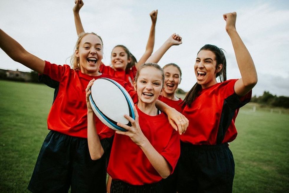 A group of girls on a field holding a rugby ball and in a celebratory mood