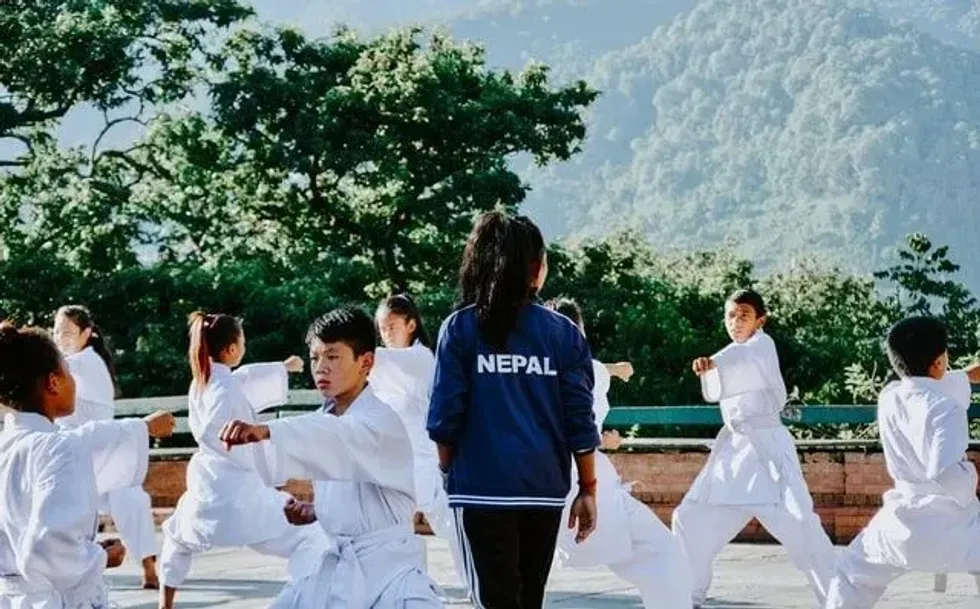 A group of kids dressed in white doboks practicing Taekwondo stances with an instructor supervising.