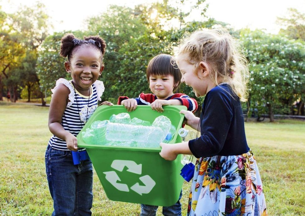 A group of kids holding a recycling bowl containing empty bottles.