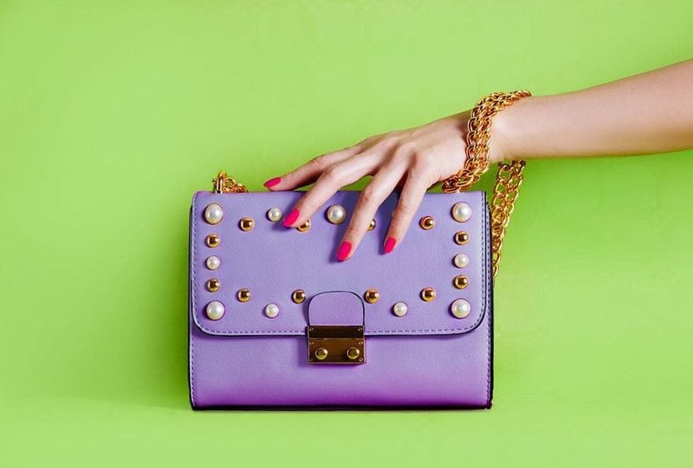A hand holding a purple purse on a green background.