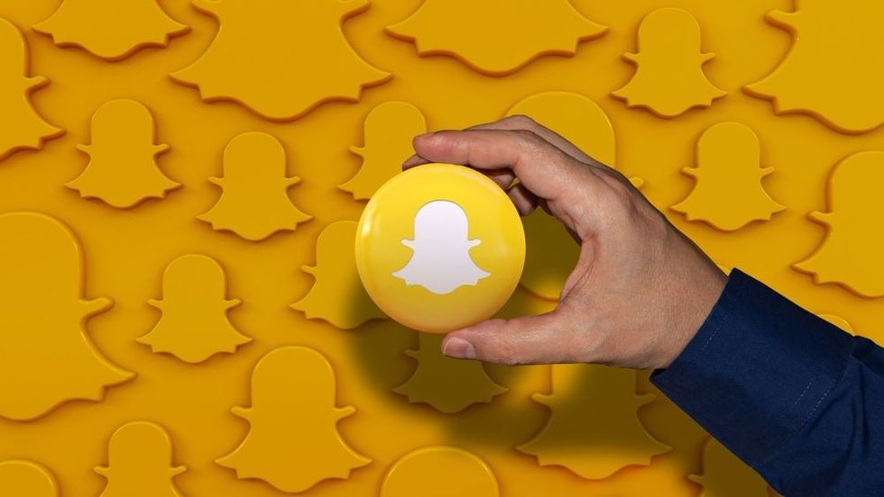 A hand holding an Snapchat logo glossy badge over orange background