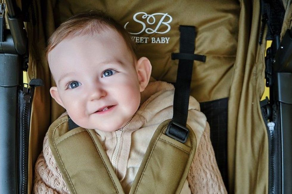 A happy child is sitting in a baby carriage on a studio yellow background