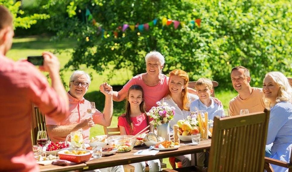 A joyful gathering of family and friends of various ages celebrating outdoors around a festive table filled with food, embodying the spirit of uniqueness and togetherness.