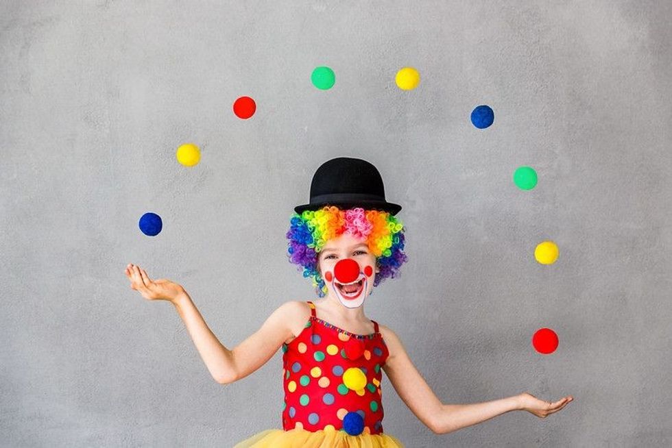 A kid dressed as a Circus Clown is juggling colorful balls in hand