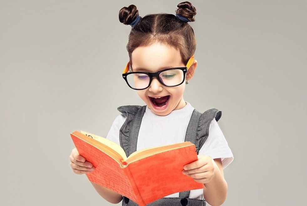 A kid in glasses looks in amazement at an orange notebook.