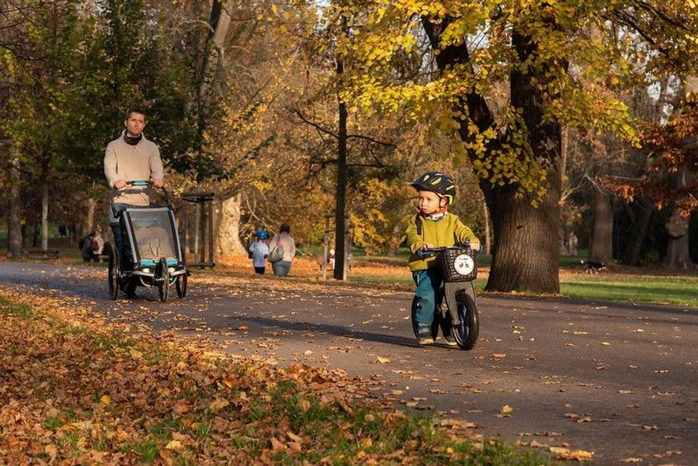 A kid is riding his motorbike in the companion of his father at the park