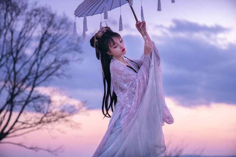A lady dressed in white attire holding a umbrella in sunset.