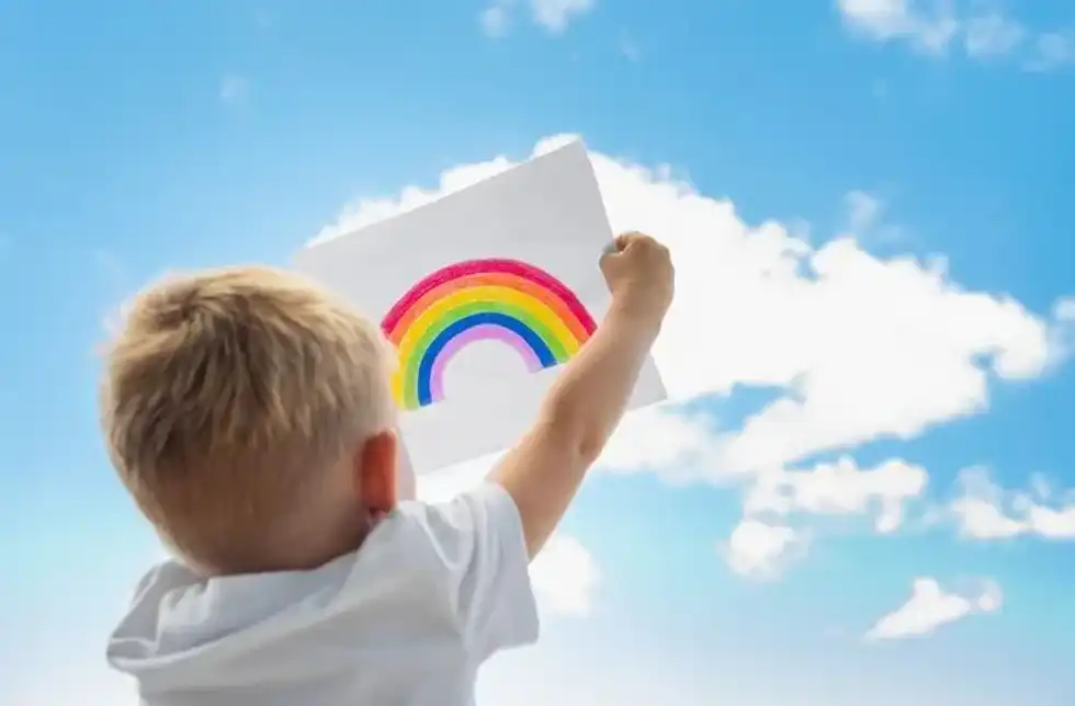 A little boy holding rainbow painting against the sky