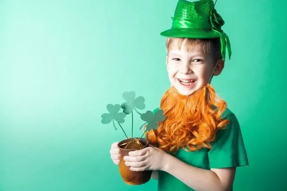 A little boy in a hat holds a small clay pot with gold coins