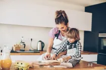 A little boy sat on the kitchen counter helping his mother making Smarties cookies.