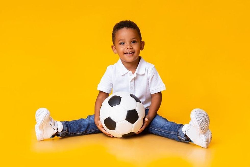 A little boy sitting with a football on yellow background