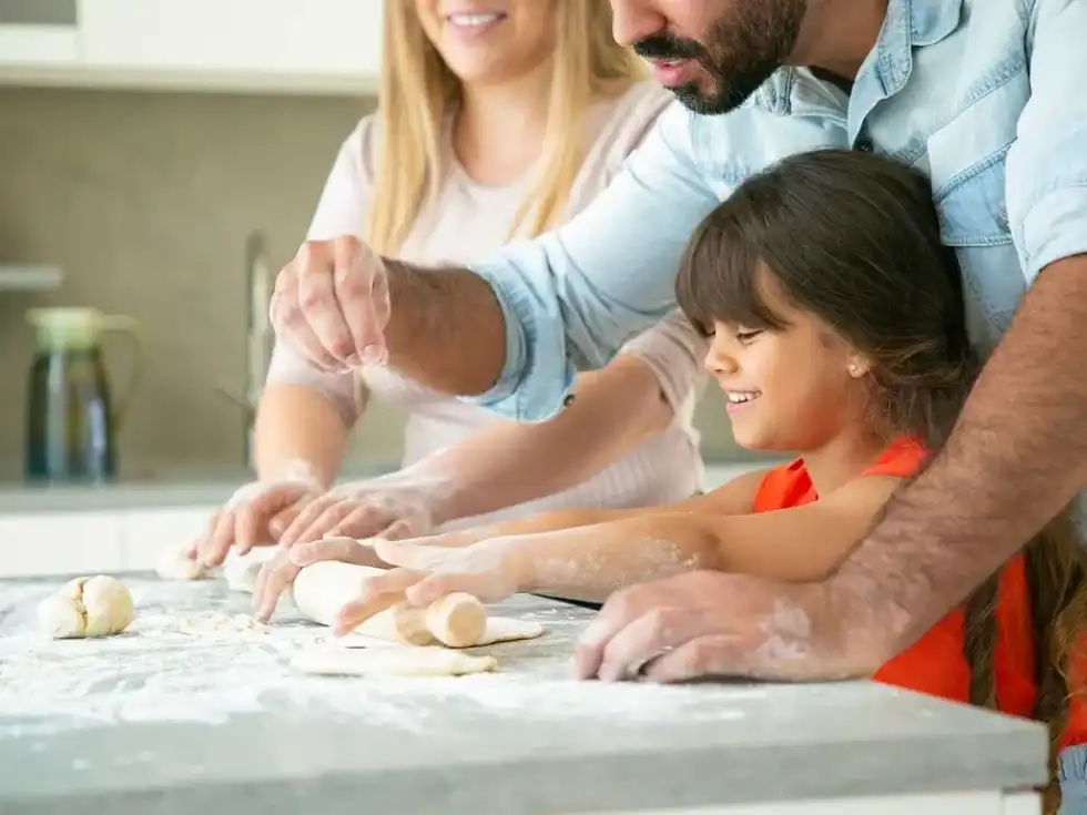 A little girl is helping her parents to roll out fondant icing to decorate a tractor cake.