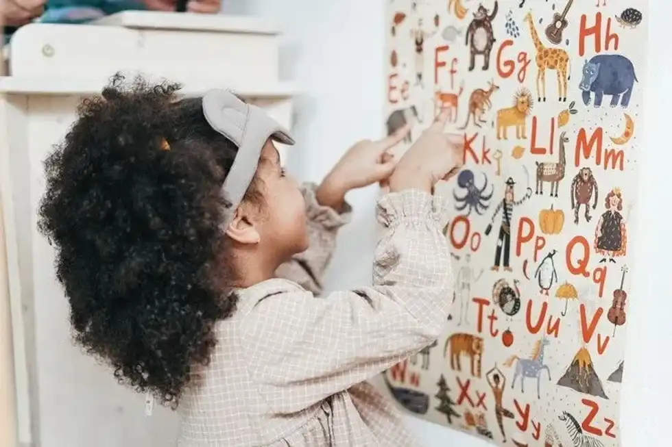 A little girl learning alphabets from a chart