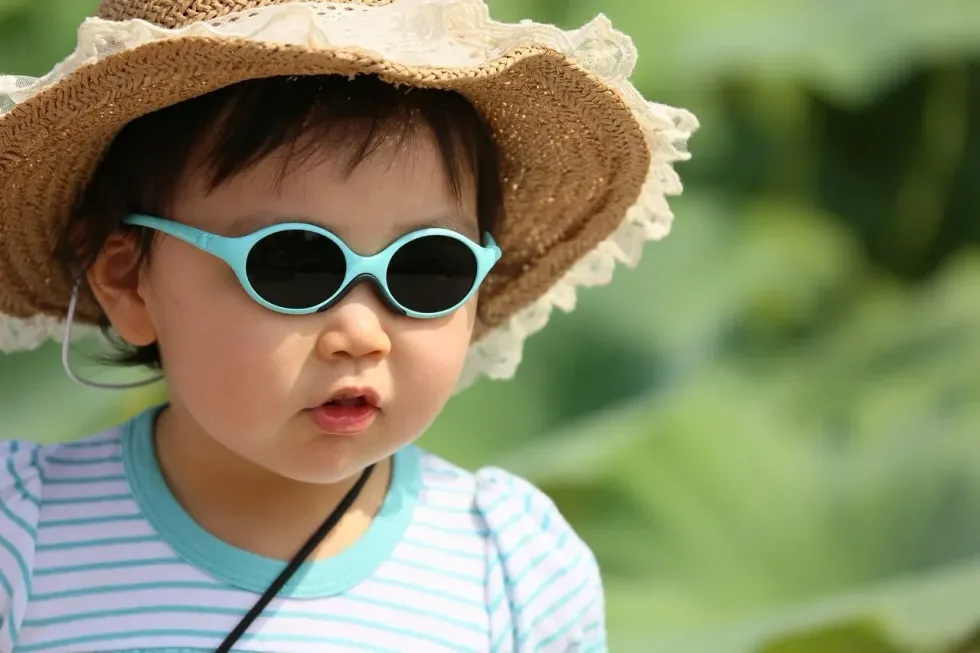 A little girl wearing blue sunglasses and woven hat