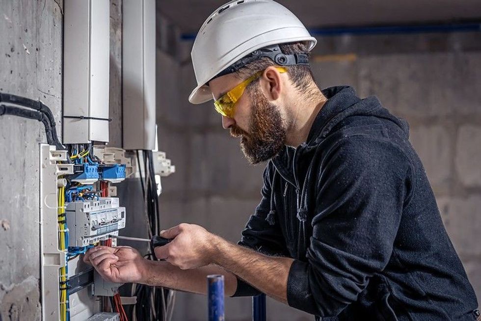 A male electrician works in a switchboard with an electrical connecting cable