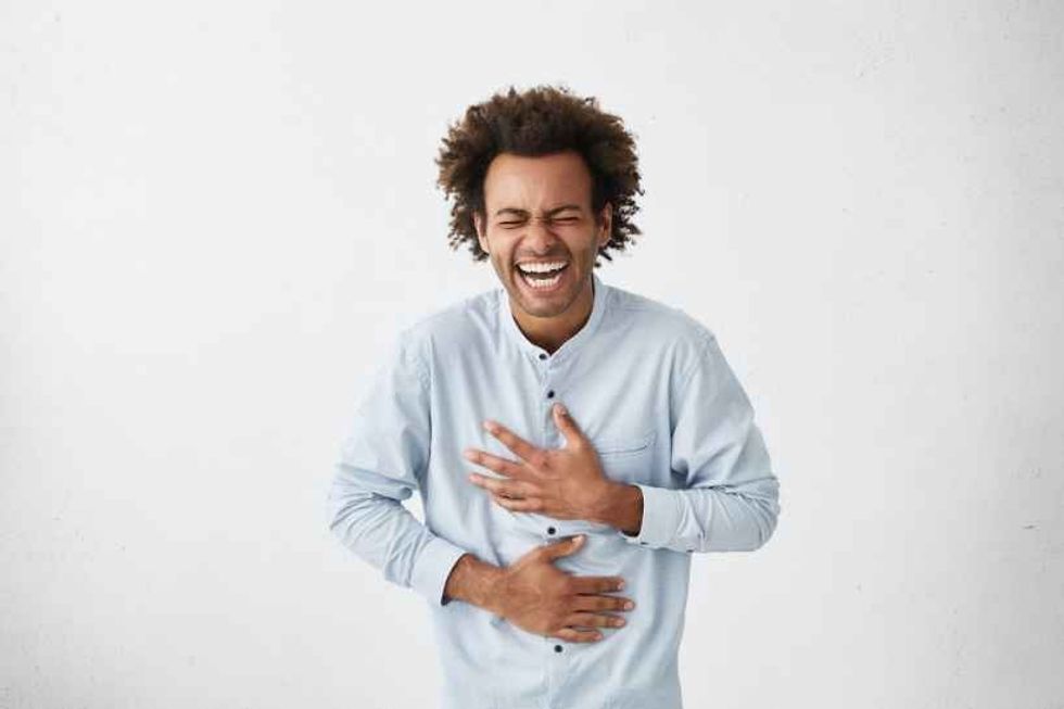A man with curly hair laughing heartily, possibly after falling for pun traps.