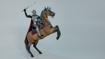A medieval knight in shining armor with a sword in a helmet with a lowered visor riding a war horse.